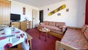 A cozy living room with a sofa, a coffee table, a television, and a snowboard on the wall. - 100m from ski slopes, 7th floor, balcony, tv, ski locker, 30m², Les Menuires (Les Menuires)