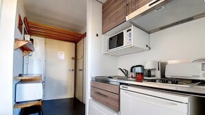 A compact kitchen with a microwave, coffee maker, and a small stove. There is a wooden shelf and a stool in the corner. - 100m from ski slopes, 7th floor, balcony, tv, ski locker, 30m², Les Menuires (Les Menuires)