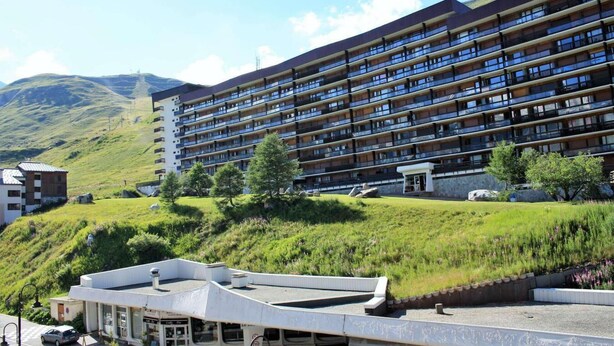 Un hotel de varios pisos con balcones, un estacionamiento y un paisaje con césped y árboles.