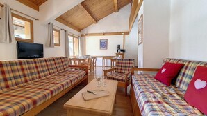 Ein gemütliches Wohnzimmer mit Karomöbeln, einem Holztisch und einem an der Wand montierten Fernseher.
