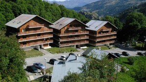 A multi-story wooden building with balconies, surrounded by lush greenery and mountains in the background. - 4th floor, swimming pool, balcony, tv, ski locker, 46m², Valloire (Valloire)