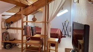 A cozy loft bedroom with a sloped ceiling, wooden beams, a bookshelf, a TV, and a bed with patterned bedding. - 4th floor, swimming pool, balcony, tv, ski locker, 46m², Valloire (Valloire)