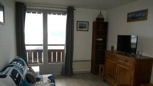En stue med en sofa, et fjernsyn på et træskab, en bogreol og en skydedør, der fører ud til en balkon.