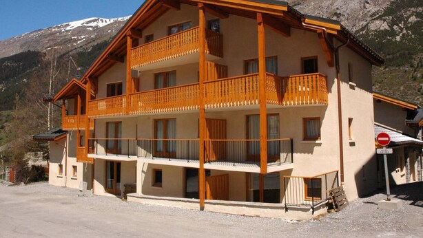Un hôtel à plusieurs étages doté de balcons, situé dans un décor de station de ski, avec un panneau indiquant qu’il est interdit de se garer.
