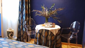 A hotel room with a bed, a round table with a vase and tea set, and two clear chairs. - Residenza San Faustino (Verona)