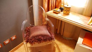 A clear chair with a frilly cushion, a wooden desk with a lamp, and a white appliance. - Residenza San Faustino (Verona)