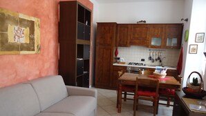 Ein Wohnzimmer mit einer Couch, einem Esstisch mit Stühlen und einer Küchenzeile mit Holfschränken und einem Herd.