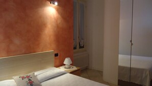 Ein Hotelzimmer mit Bett, Nachttisch, Lampe und einem Fenster mit Vorhängen.