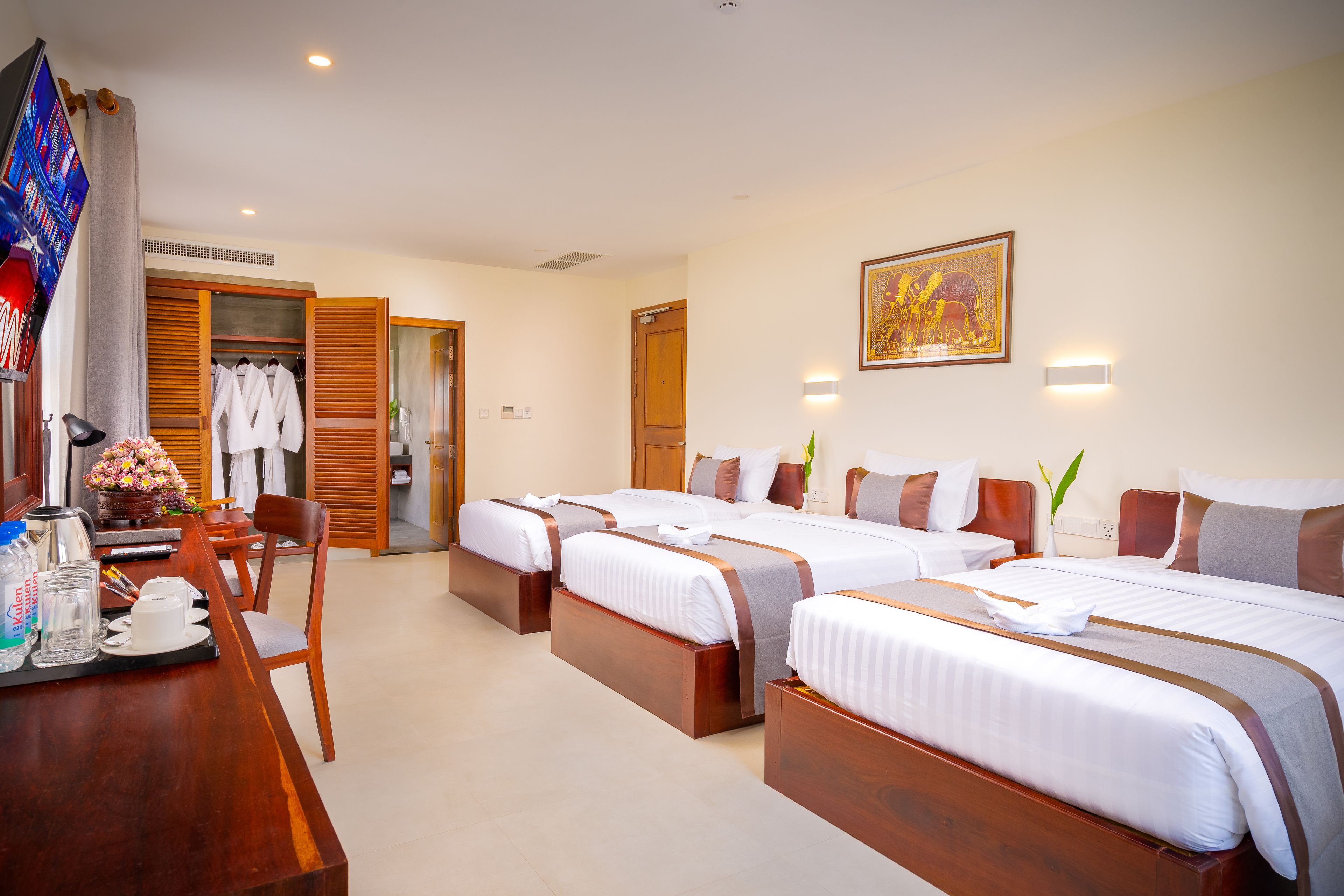 A hotel room with three beds, a desk with a coffee maker, and a TV.