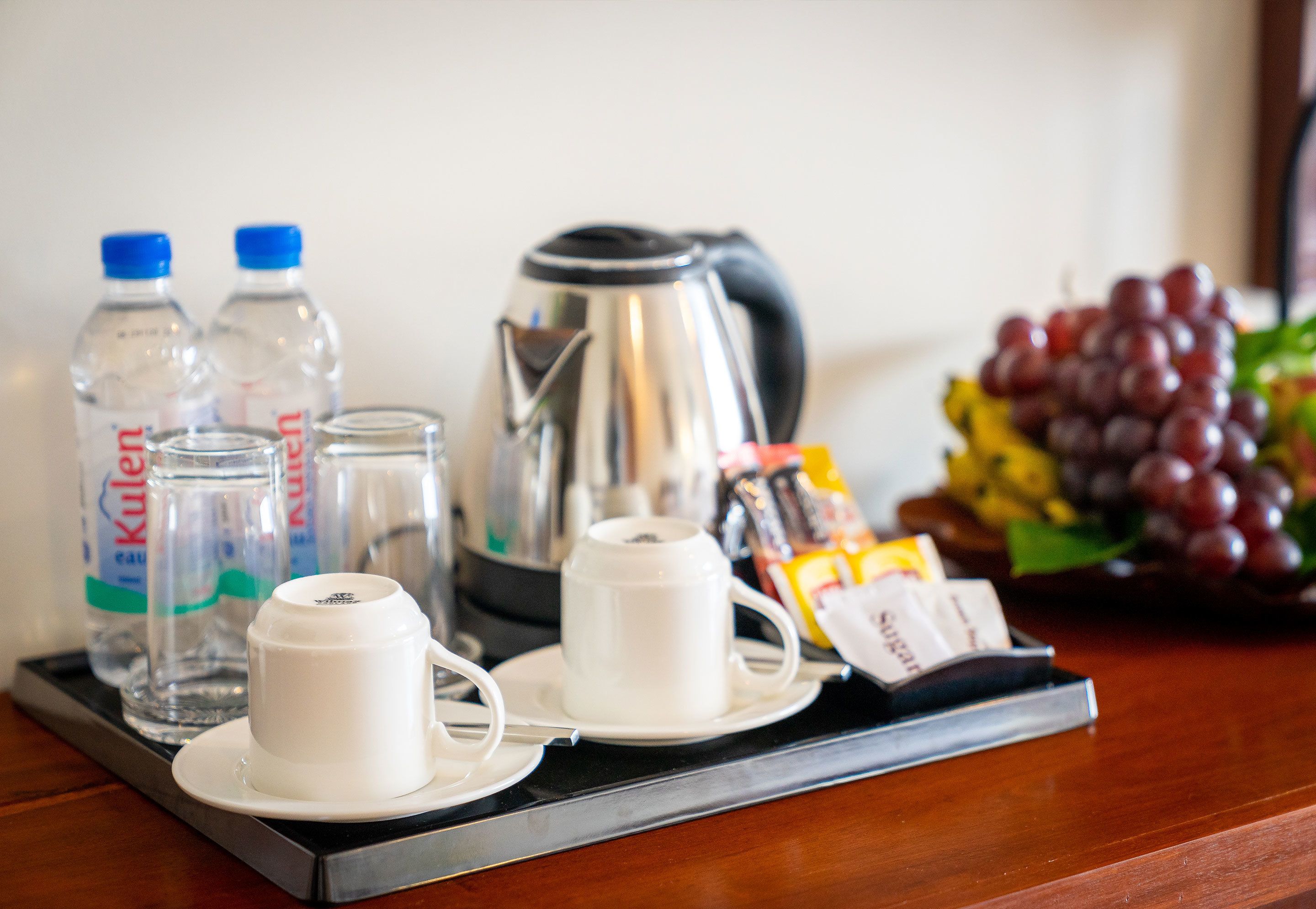 A tray with a coffee maker, two cups, two bottles of water, a packet of sugar, and a bunch of grapes.