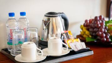 A tray with a coffee maker, two cups, two bottles of water, a packet of sugar, and a bunch of grapes.