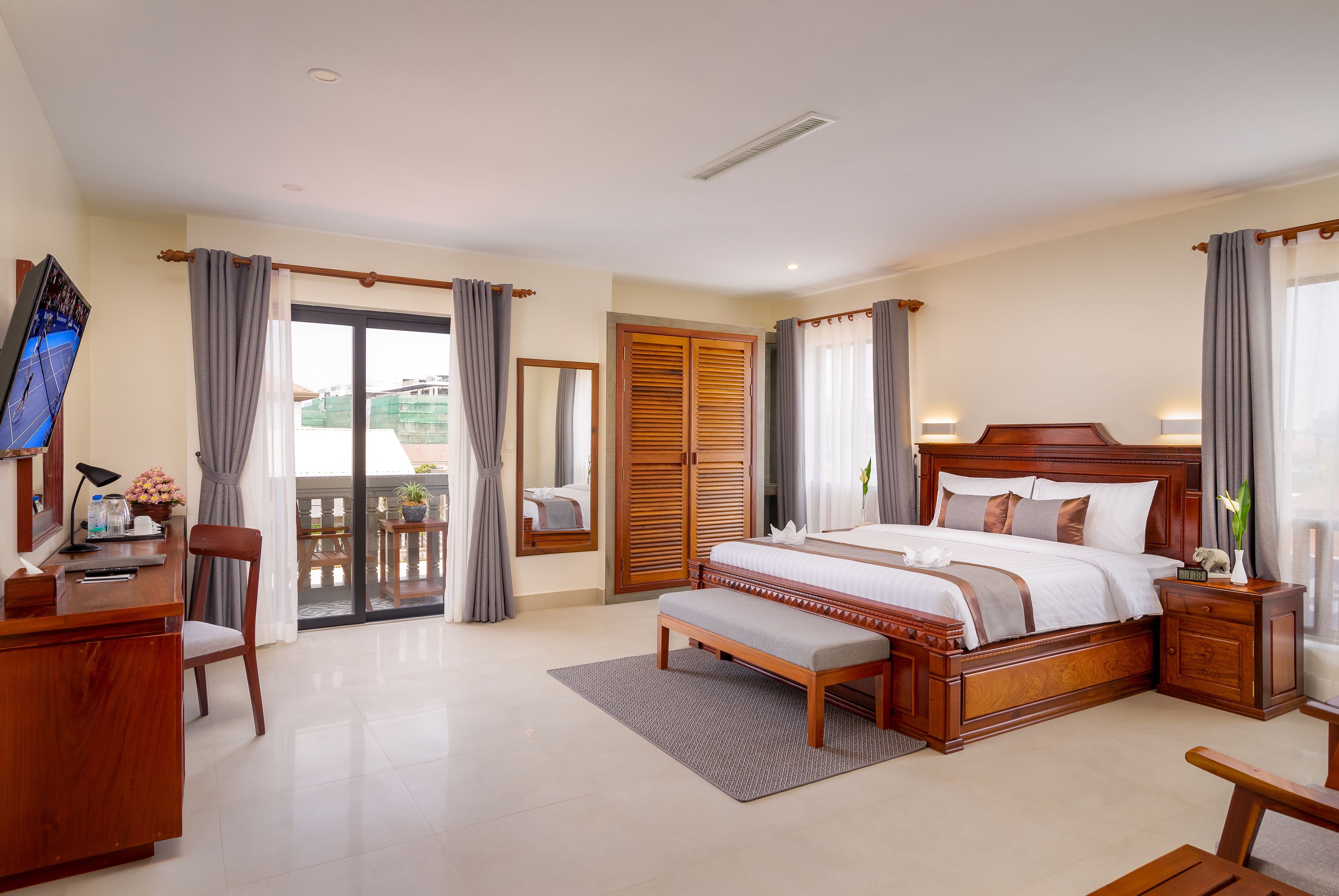 A spacious bedroom with a large bed, wooden furniture, a desk, and a balcony with curtains.
