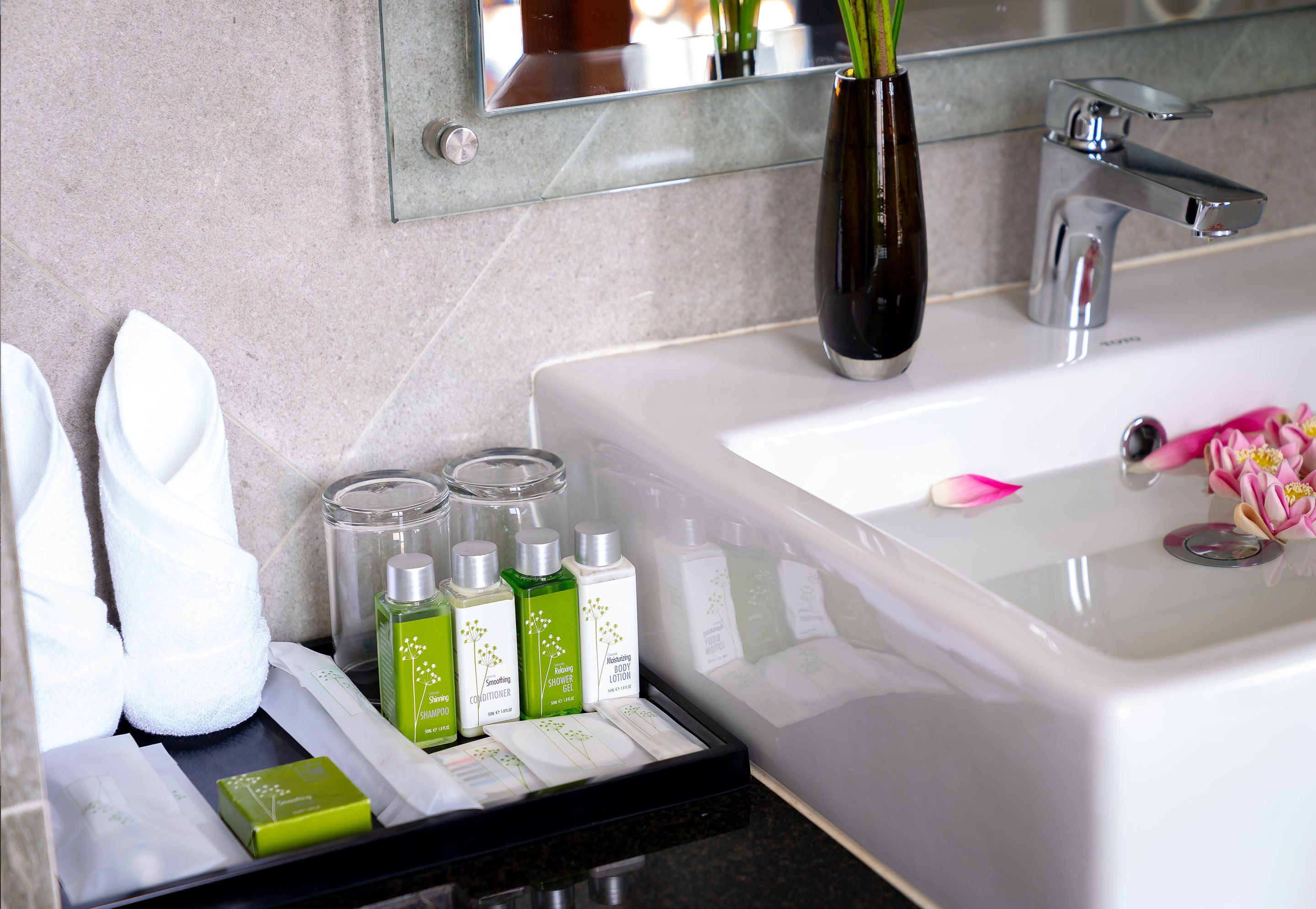 Een badkamer met een witte wastafel, een spiegel en toiletartikelen zoals shampoo, conditioner en lotion.