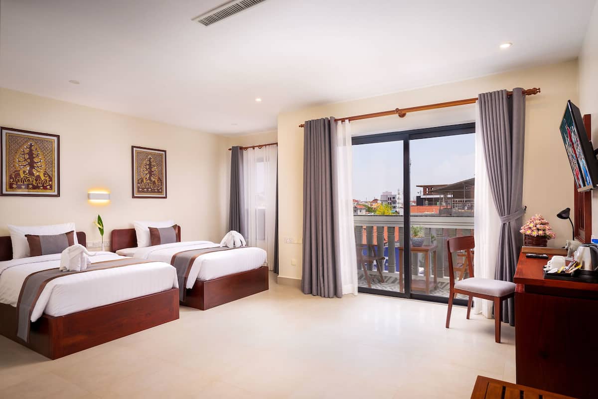 A hotel room with two beds, a desk, a chair, and a balcony with a view.