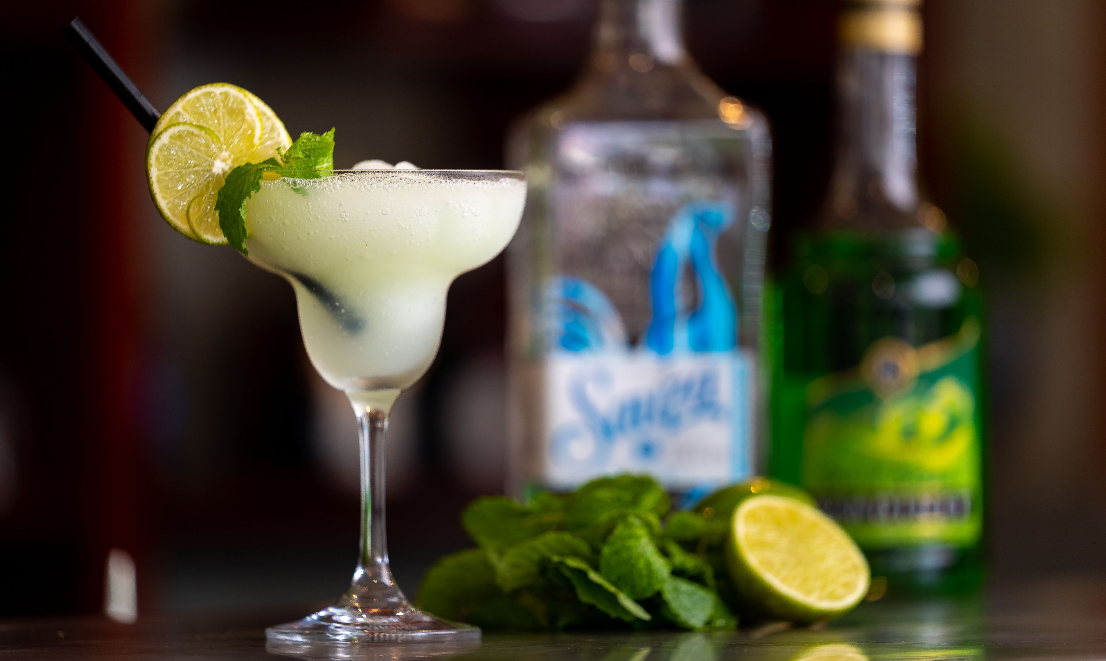 Un cocktail con guarnizione al lime, una bottiglia di vodka Smirnoff e una bottiglia di acqua tonica verde.