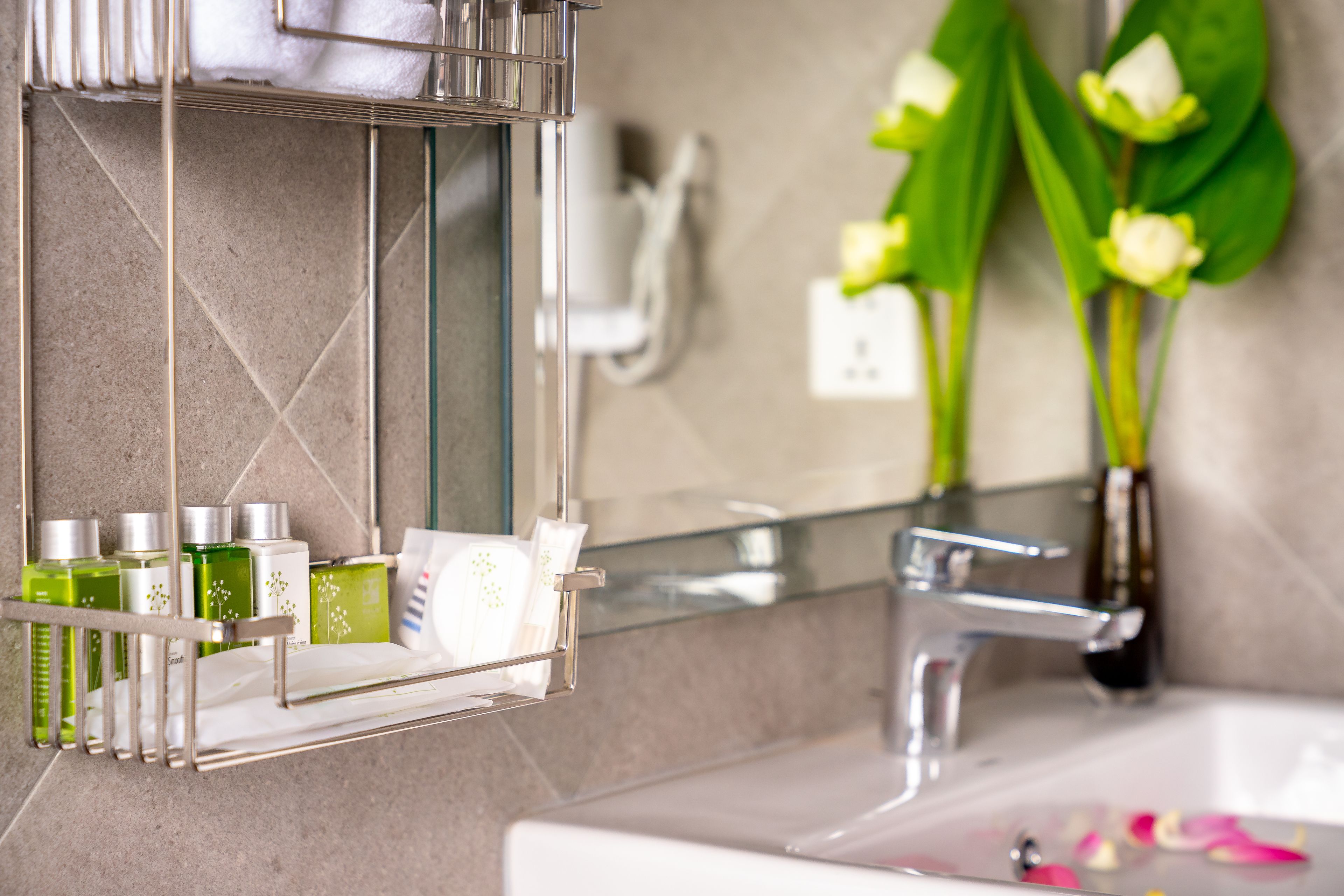 A bathroom with a glass shelf holding toiletries, a mirror, and a sink with rose petals.
