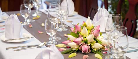Mesa dispuesta para un evento de cena formal, con manteles blancos, cristalería transparente y un centro de mesa con flores rosa y blancas.
