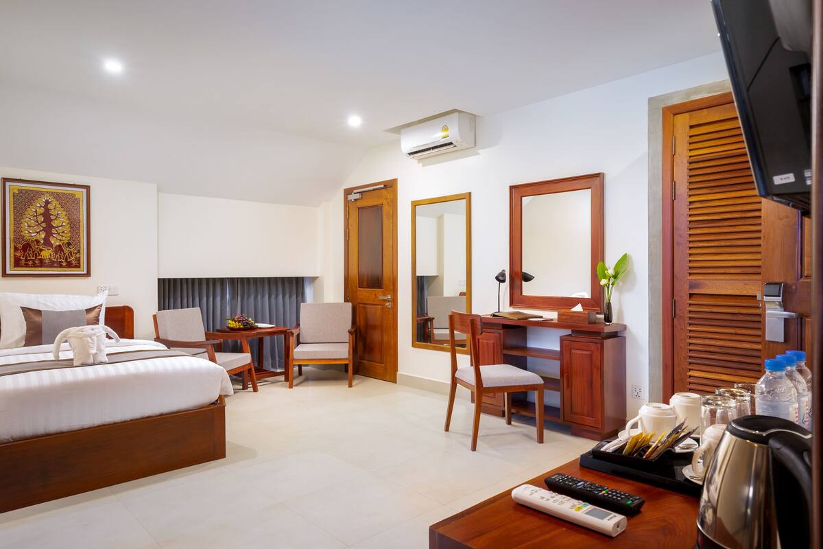 A hotel room with a bed, two chairs, a desk, a TV, a coffee maker, and a mirror.
