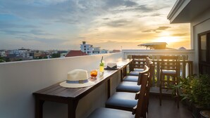 Eine Dachterrasse mit Holztisch, Stühlen und Blick auf den Sonnenuntergang über der Stadt.