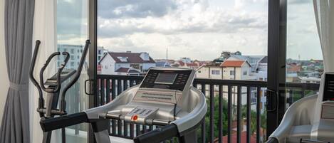 Un gimnasio en casa con cinta de correr y máquina elíptica, un balcón con vistas a edificios y un suelo estampado.