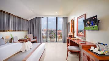 Habitación de hotel con una cama grande, un escritorio, televisor y un balcón con vistas a edificios.