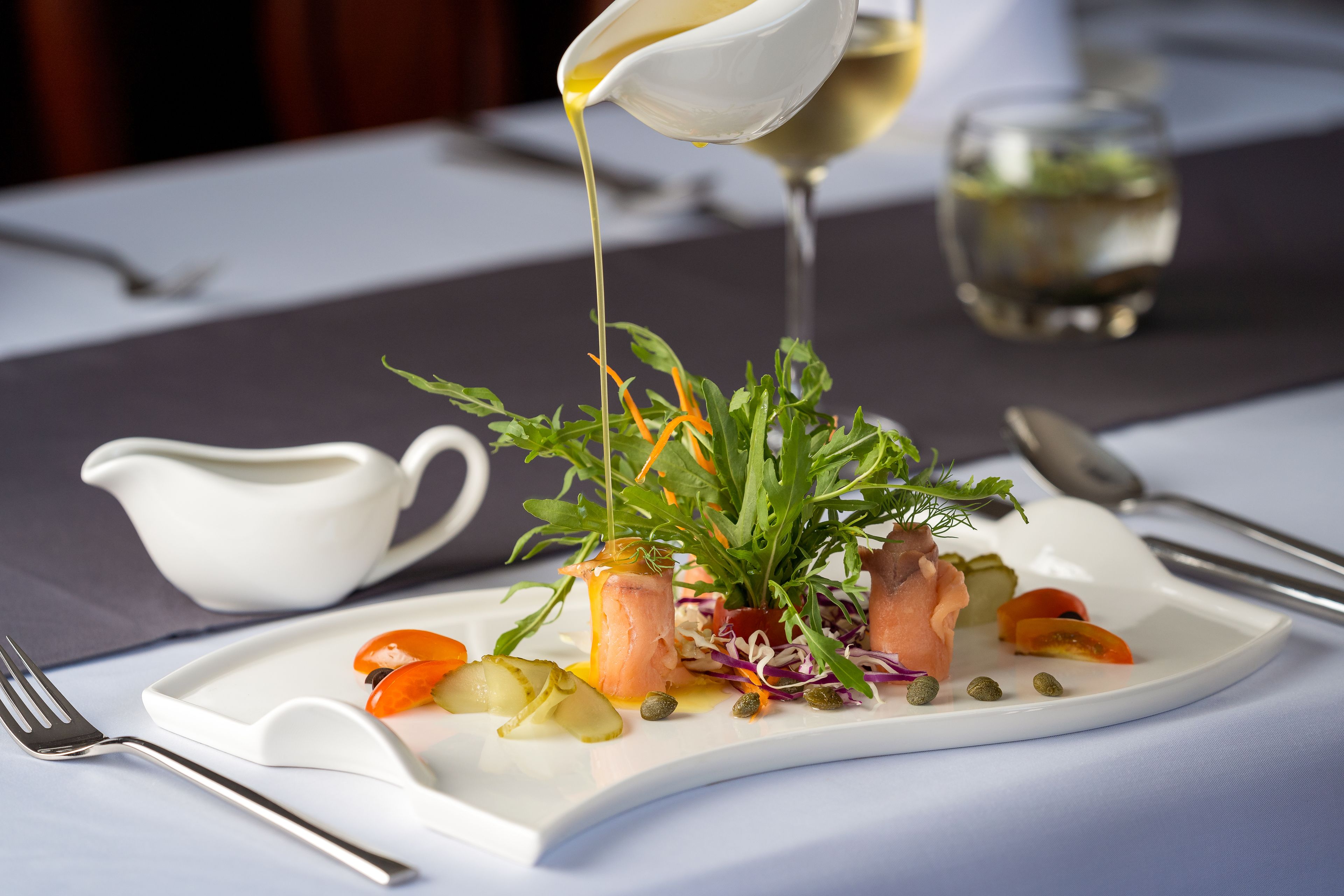 A white plate with a salad, a white pitcher, and a glass of white wine on a table.