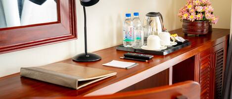 A wooden desk with a lamp, water bottles, a coffee pot, and a flower vase.