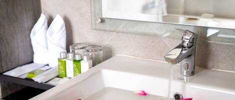 A bathroom with a white sink, a mirror, and toiletries on a shelf.