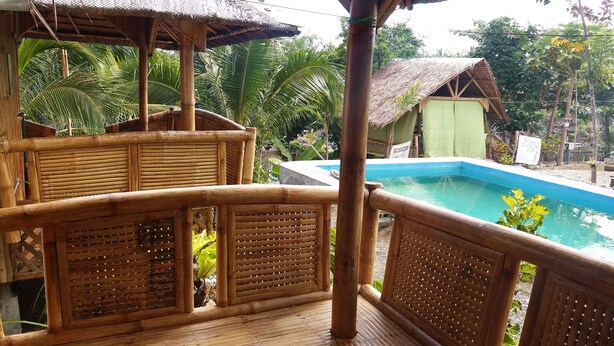 A wooden deck with a pool, surrounded by lush greenery and a thatched-roof structure. - Villa Catalina Bora Resort (Nabas)