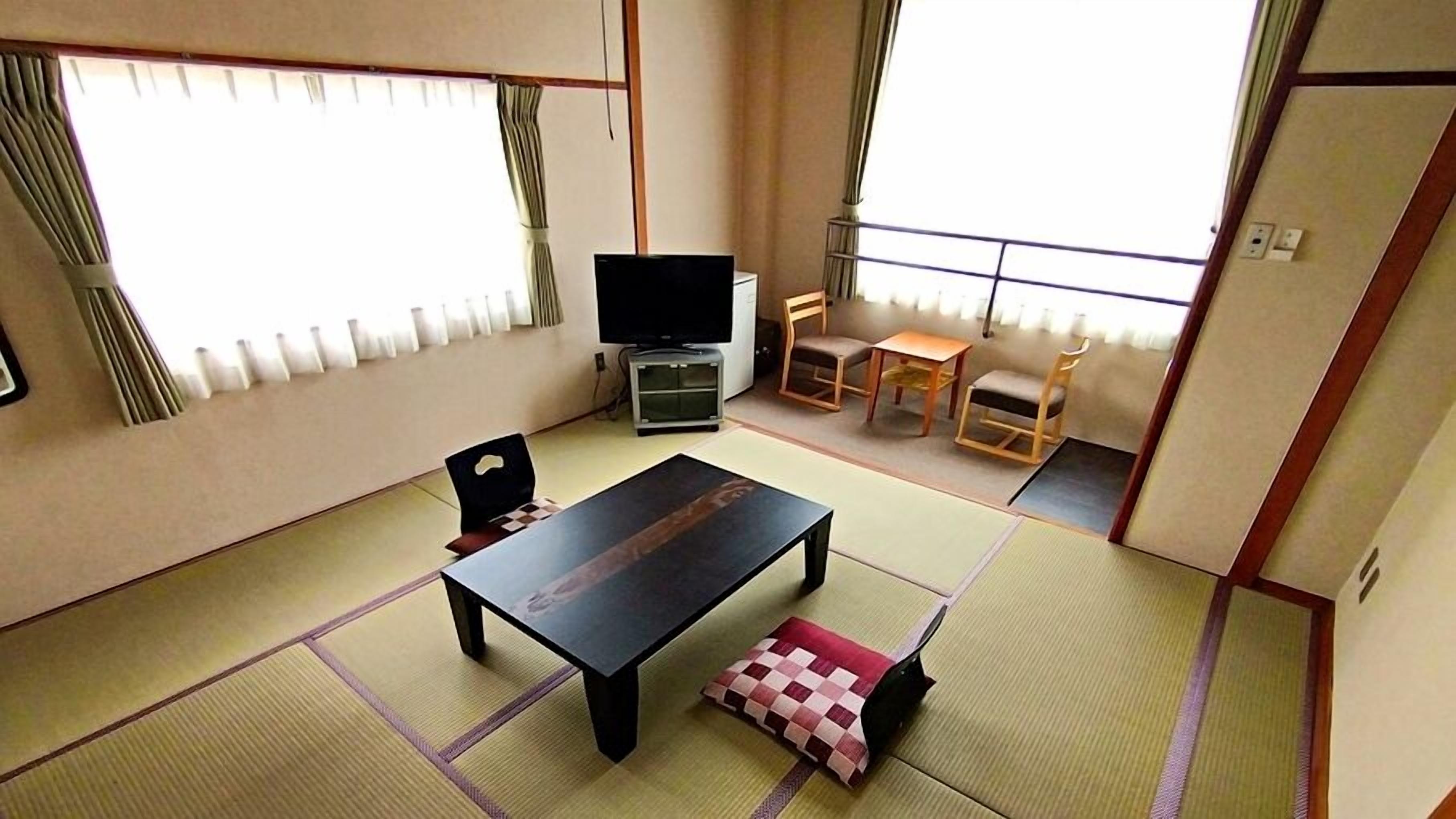 Quarto japonês tradicional com tatames, uma mesa baixa, uma televisão e uma porta deslizante.
