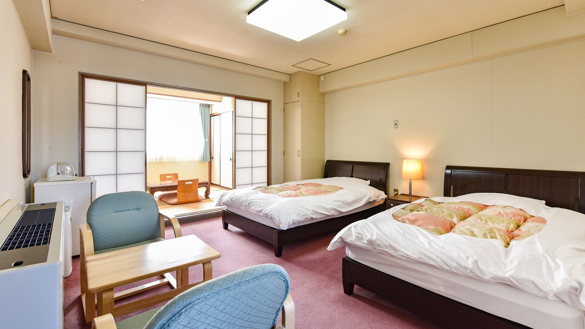 Une chambre d’hôtel avec deux lits, un bureau, une chaise, un ordinateur portable et une fenêtre donnant sur un beau paysage.