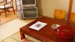 Una habitación tradicional japonesa con tatami, una mesa de madera baja, un televisor y un recipiente rojo.