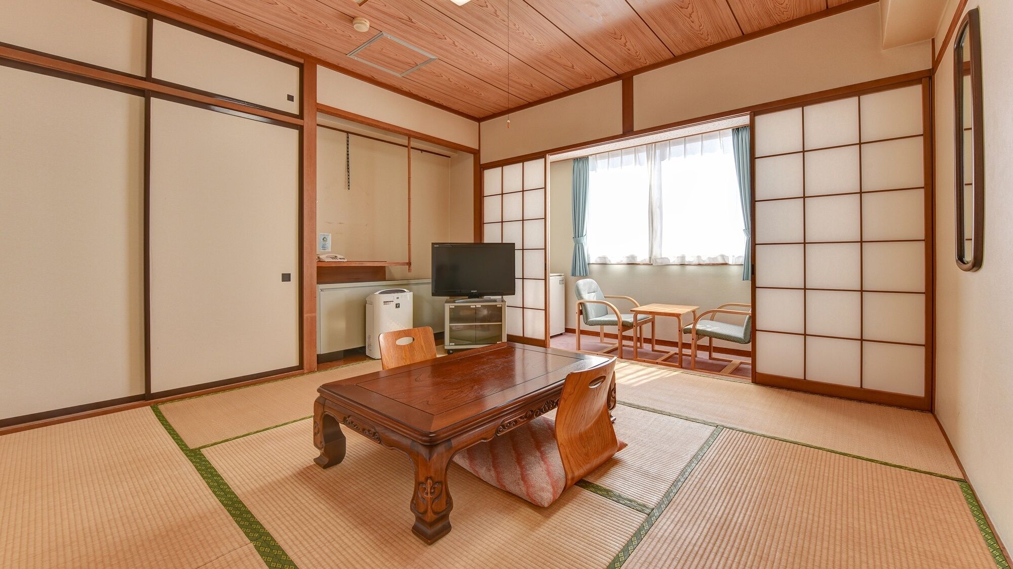 Une pièce de style japonais traditionnel, avec un sol recouvert de tatamis, une table en bois, un téléviseur et une porte coulissante.