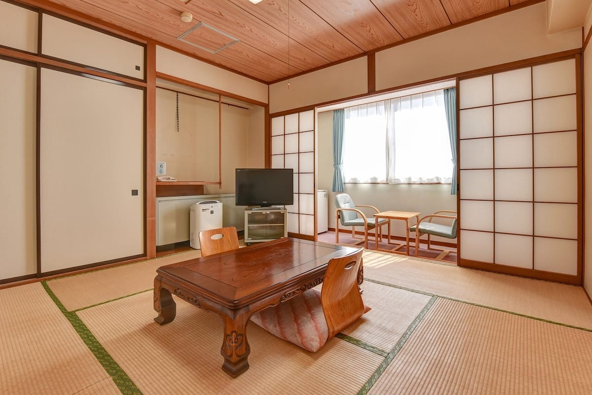 Une pièce de style japonais traditionnel, avec un sol recouvert de tatamis, une table en bois, un téléviseur et une porte coulissante.