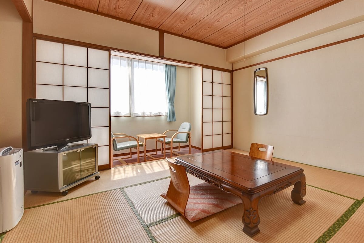 Une pièce de style japonais traditionnel, avec un sol recouvert de tatamis, une table en bois, un téléviseur et une porte coulissante.