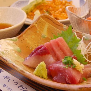 Ein Teller mit Sushi, garniert mit Frühlingszwiebeln und einem Blatt, sowie eine Schüssel Sauce im Hintergrund.