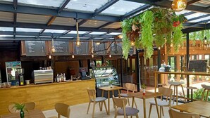 Een café met houten tafels en stoelen, een bar met een menubord, en hangende beplanting.
