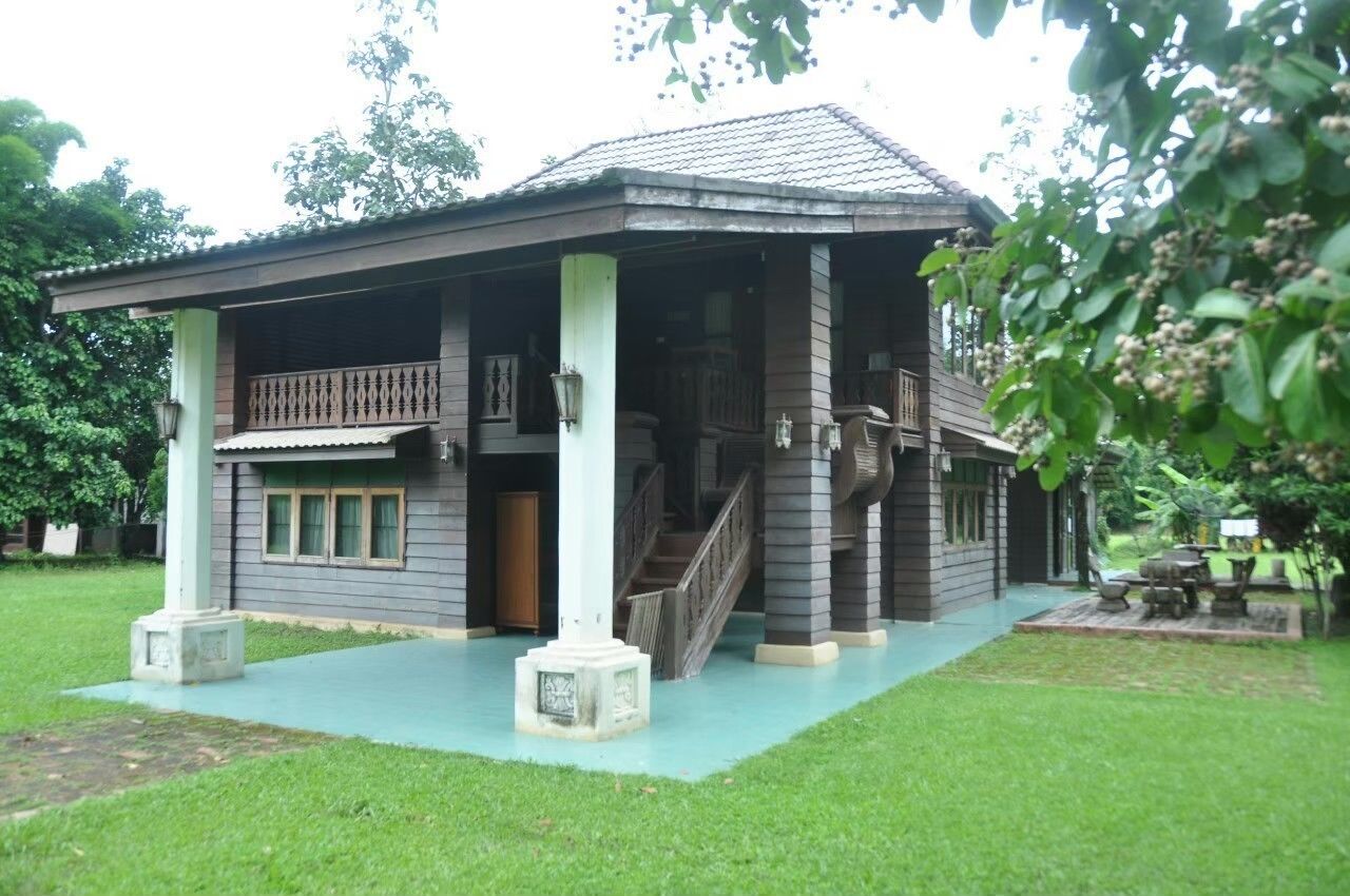 A two-story wooden house with a balcony, a staircase, and a small garden area.