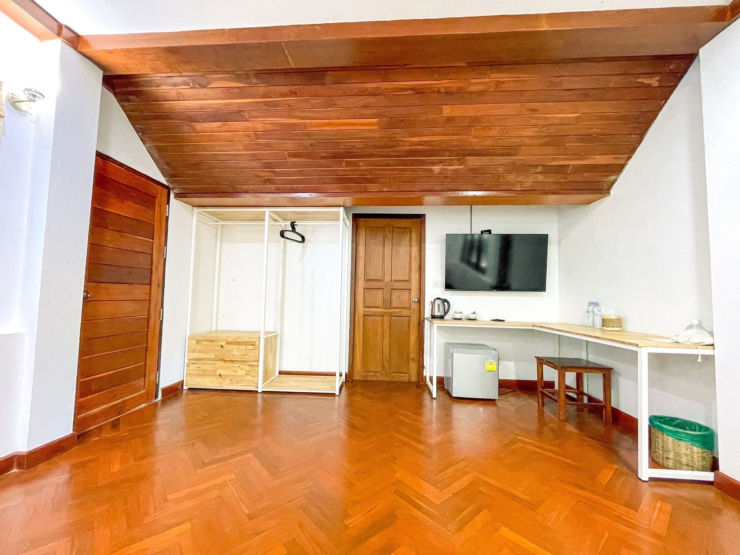 Una habitación con suelo de madera, un televisor montado en la pared, una puerta de madera y una pequeña zona de kitchenette.
