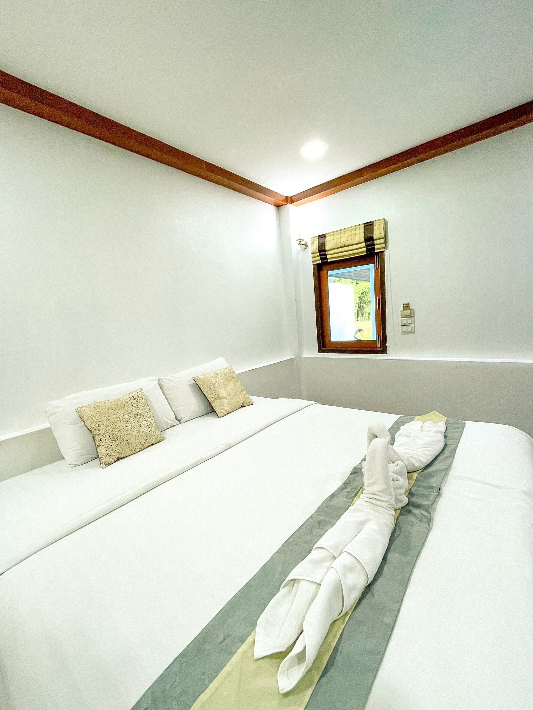 A hotel room with a large bed, white linens, a window with a view, and a wooden ceiling.