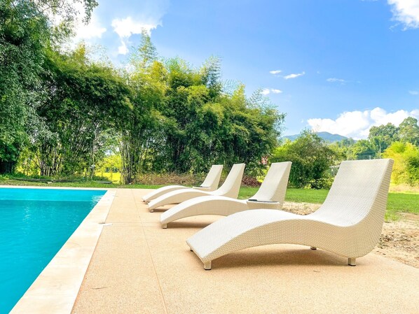 Un área junto a la piscina con sillas de descanso y una piscina azul cristalina.