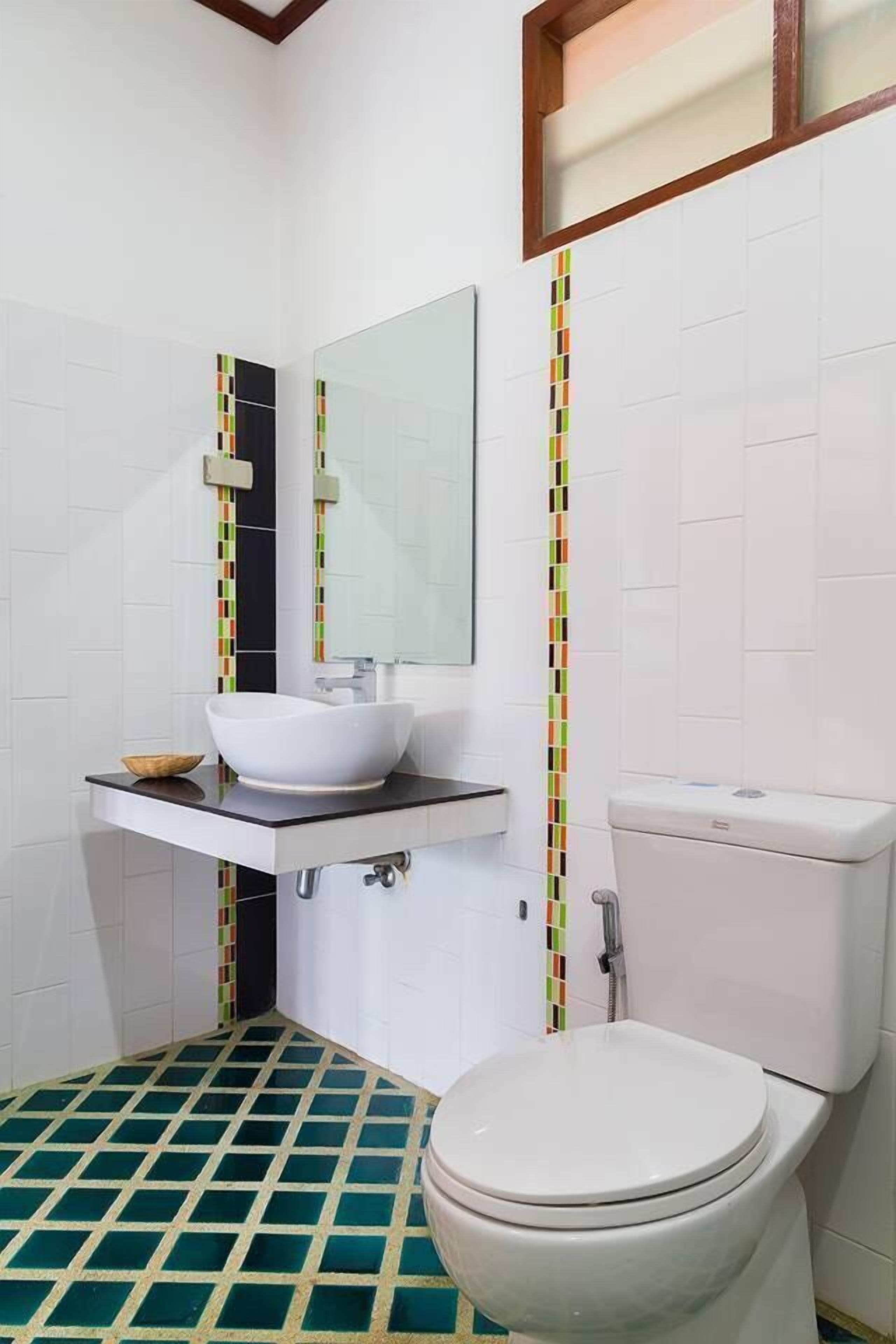 A bathroom with a white toilet, a white sink with a mirror above it, and a tiled floor with a green and white pattern.