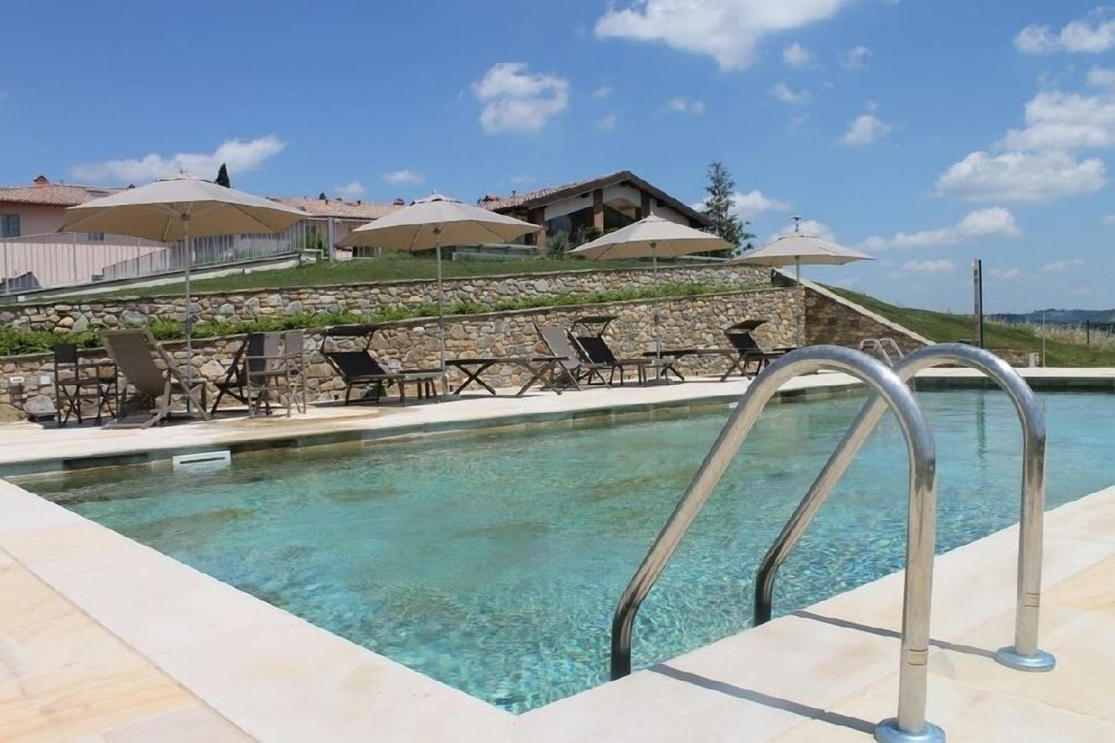 Ein Pool mit Liegestühlen und Sonnenschirmen, umgeben von Steinmauern und Blick auf eine Hügelterrasse.