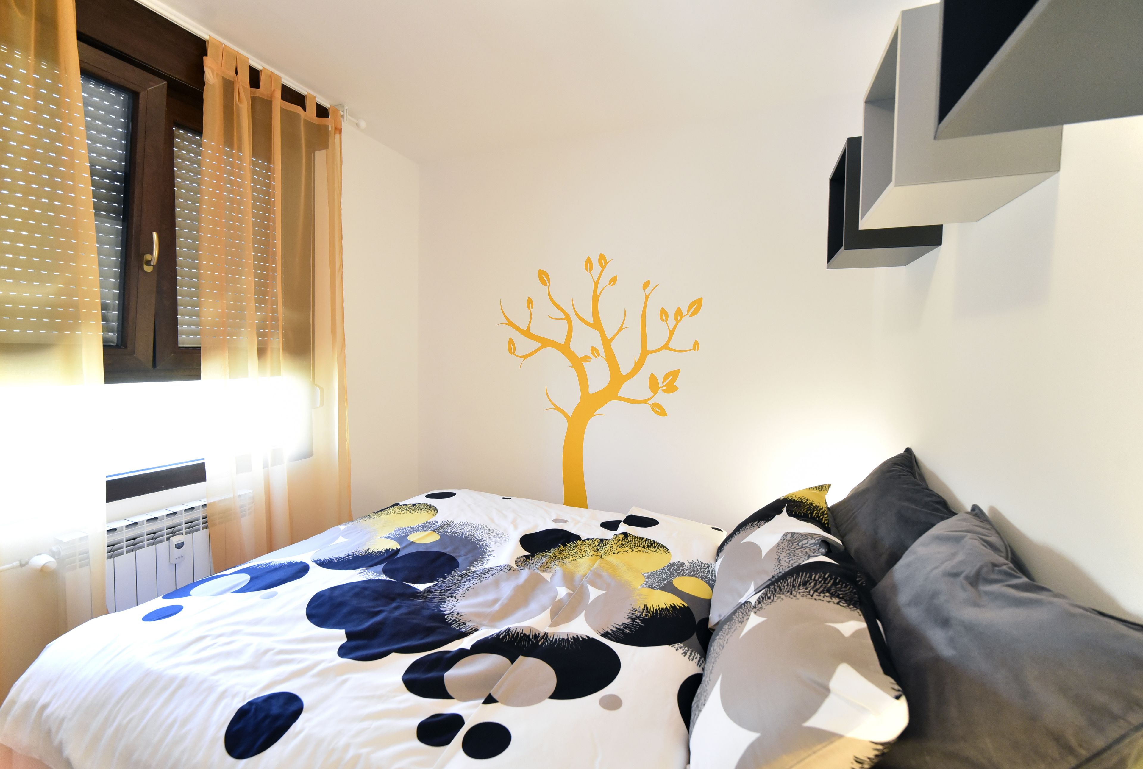 A bedroom with a bed, a tree decal on the wall, and a window with curtains.
