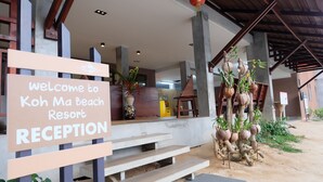Zona de recepción en Koh Ma Beach Resort, con un cartel, escalones y plantas decorativas.