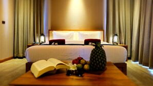 Una habitación de hotel con una cama grande, dos mesitas de noche y una mesa de madera con frutas y un libro abierto.
