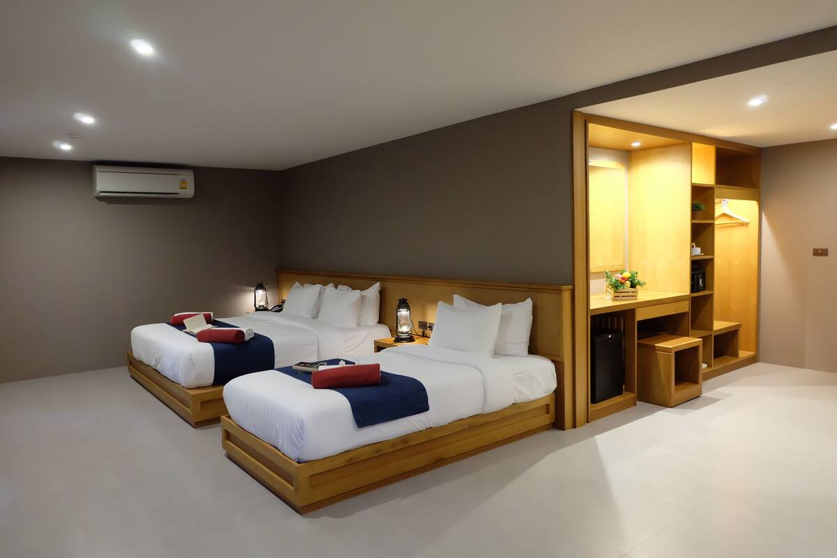 A modern hotel room with two wooden beds, a built-in wardrobe, and a ceiling-mounted air conditioner.