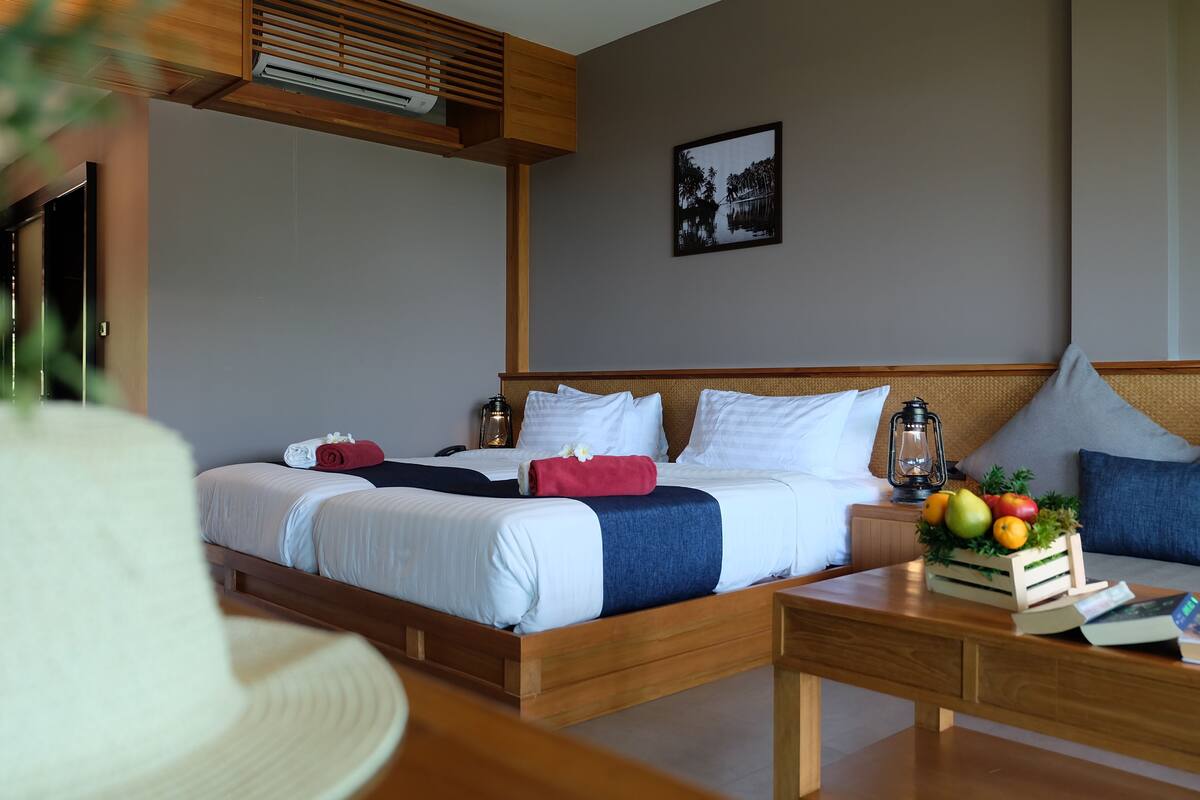 A neatly arranged hotel room with a bed, bedside tables, a small table with fruits, and a wall-mounted picture.