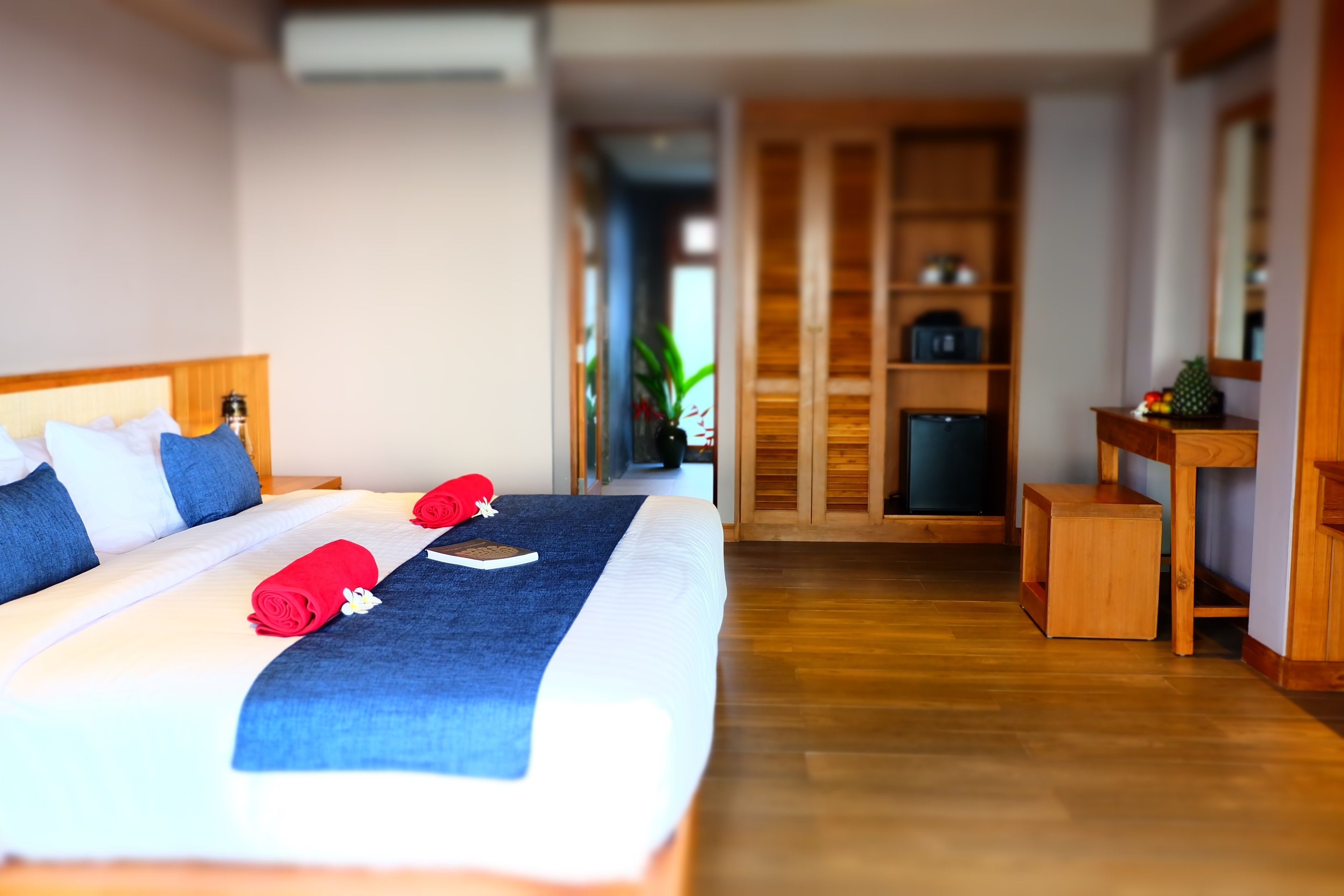 A hotel room with a large bed, a wooden desk, a small cabinet, and a wardrobe.