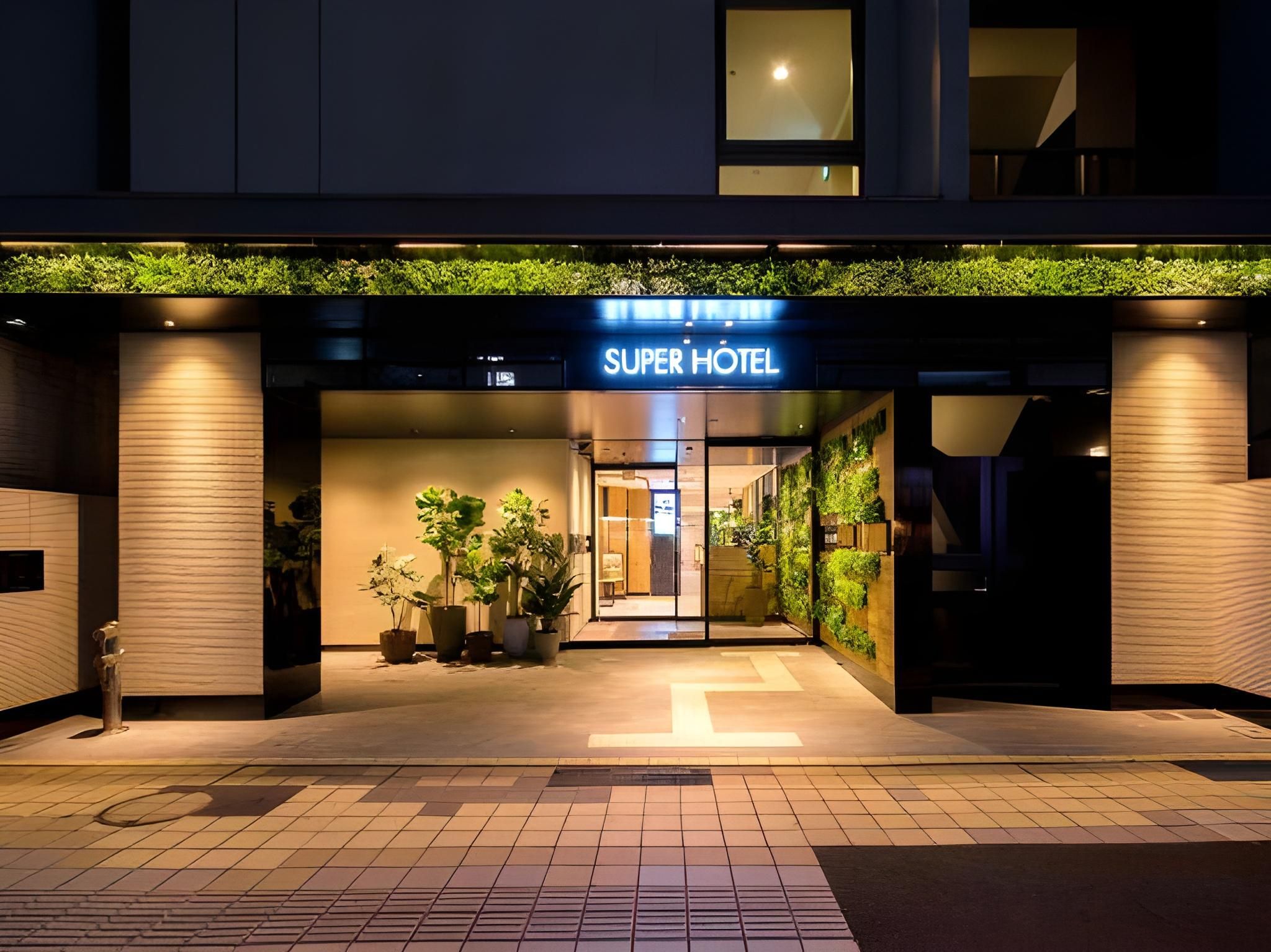 The entrance of a hotel with a sign reading 'SUPER HOTEL'. There are potted plants outside the entrance.